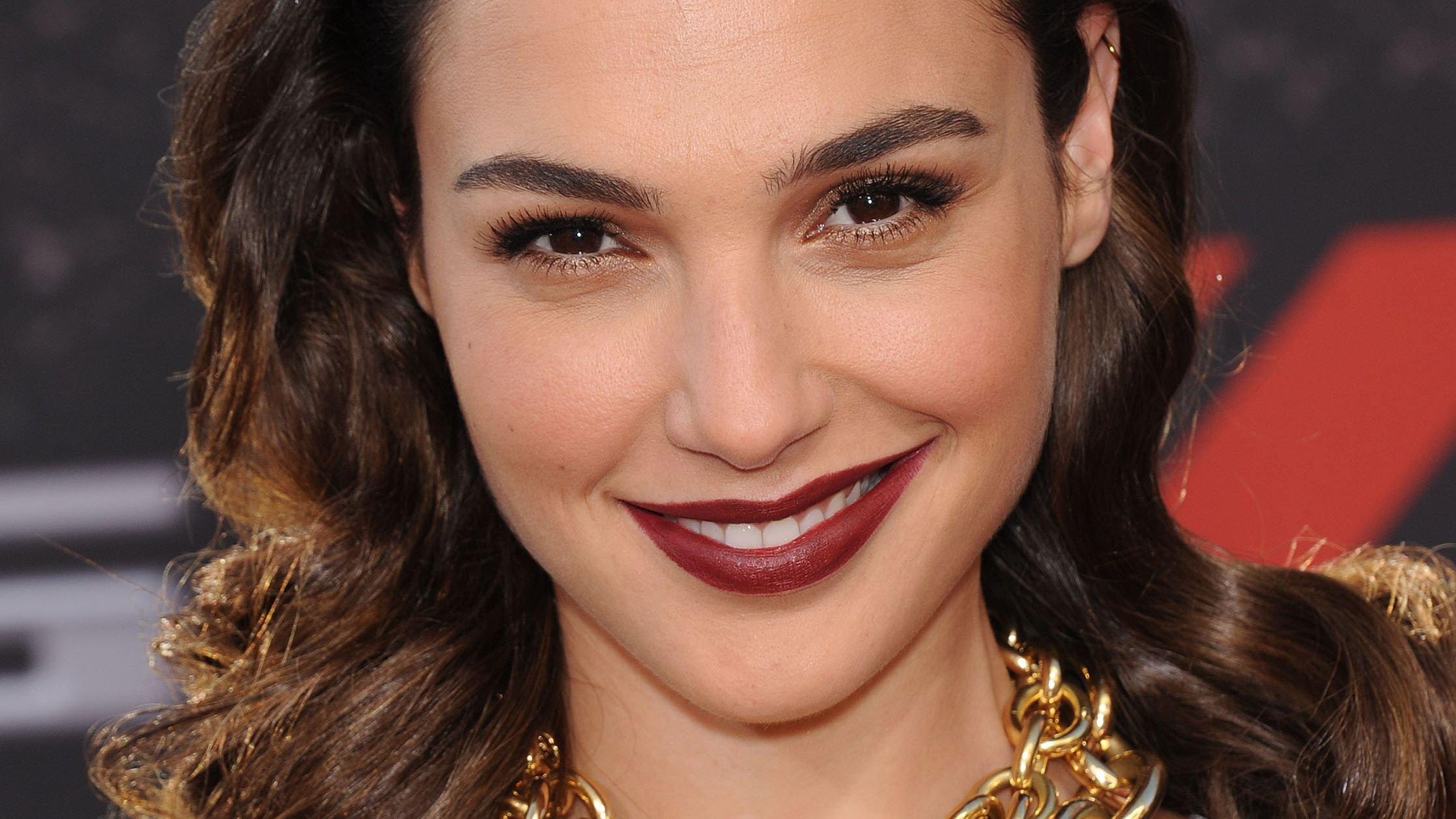 Close-up of Gal Gadot with burgundy lipstick and massive gold chain necklace.
