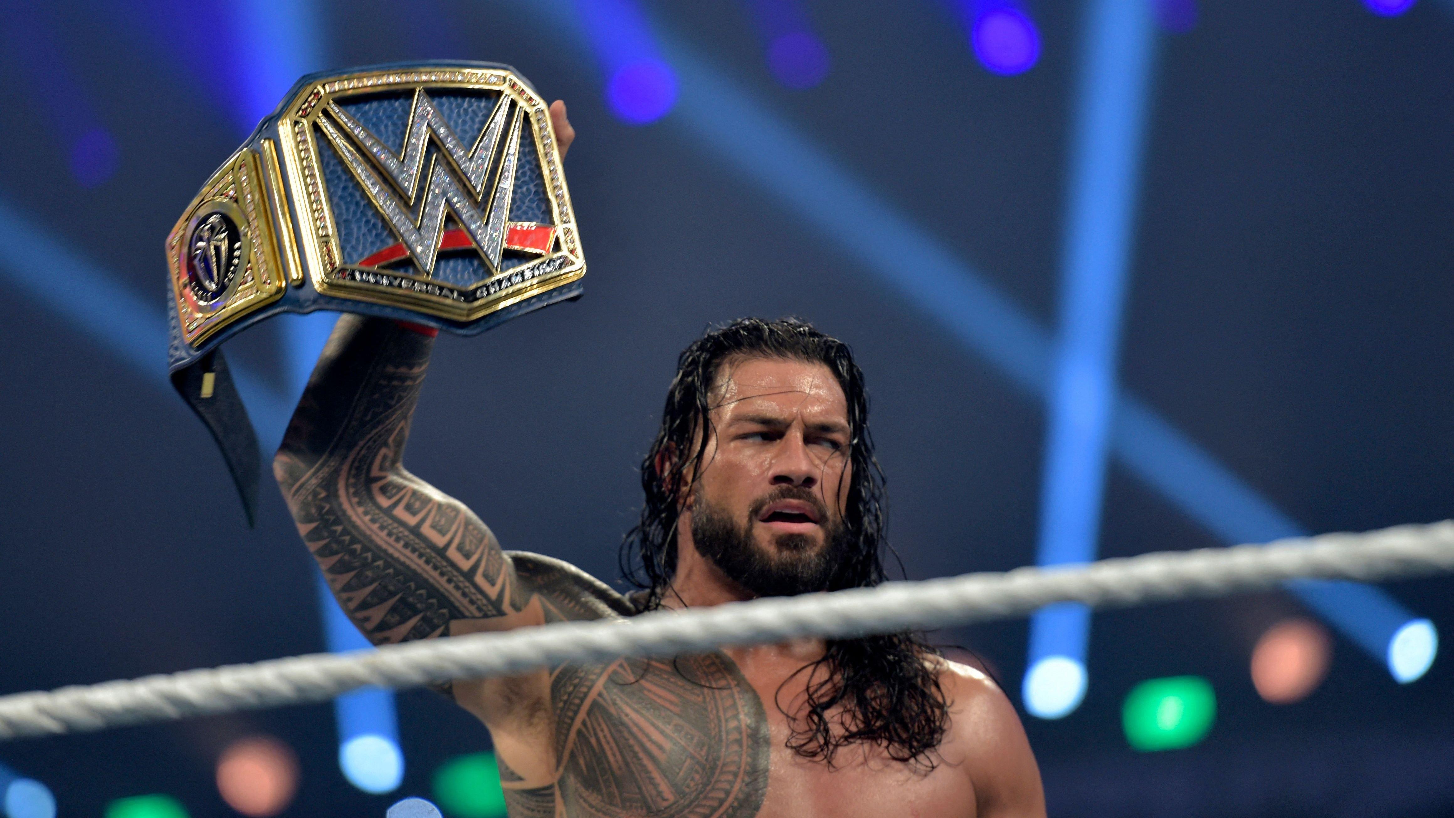 Roman Reigns standing in the WWE ring holding the WWE Universal Championship Belt 