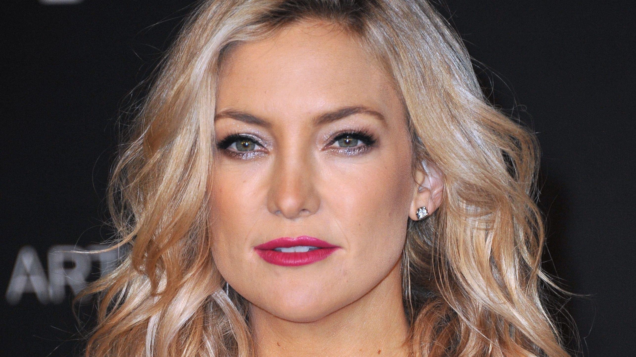 Kate Hudson with curly blonde hair and bold pink lips.