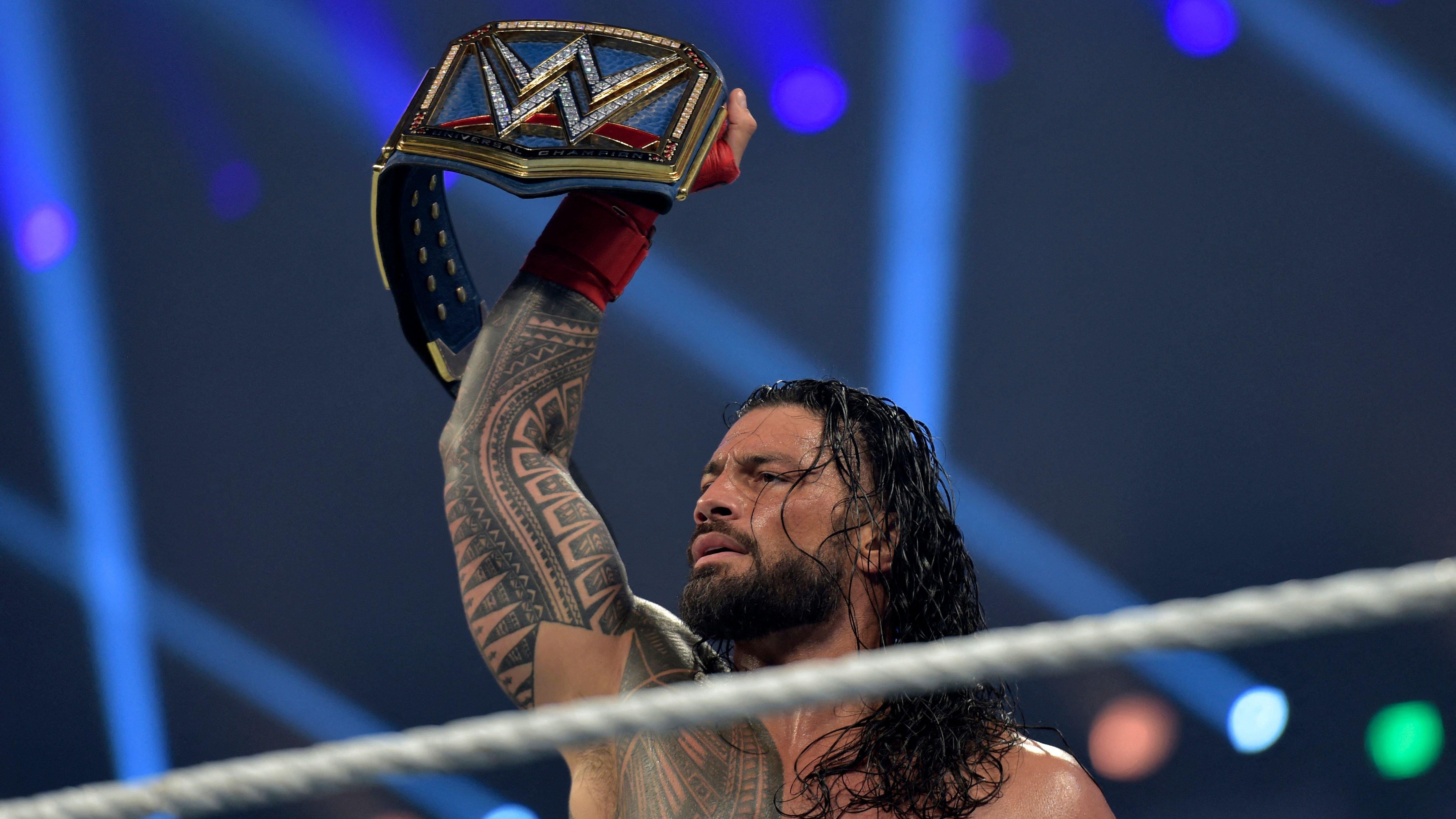 Roman Reigns holding the Universal Championship belt overhead in the WWE ring