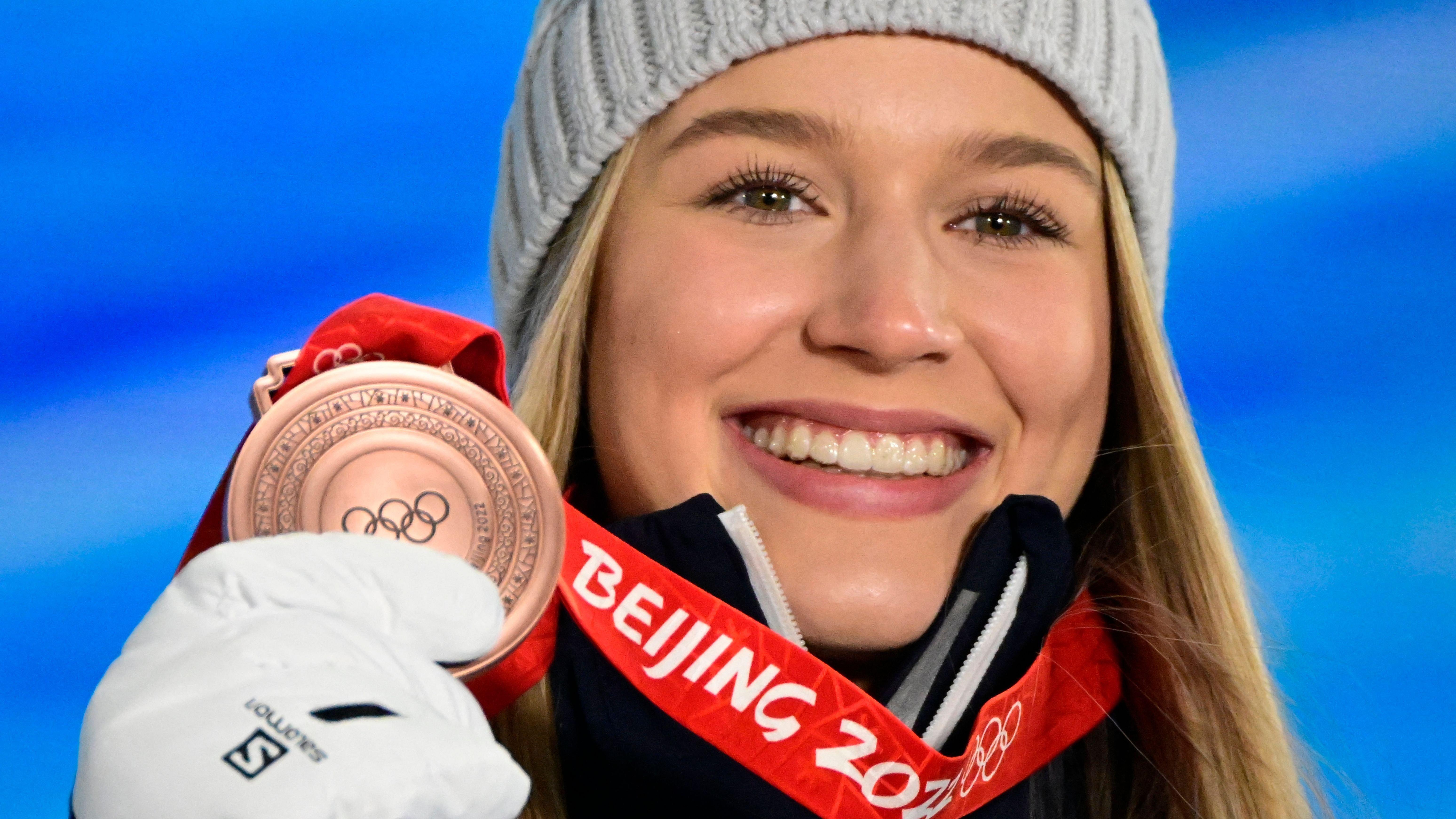 Kelly Sildaru wearing a beanie and holding up her Olympic bronze medal.