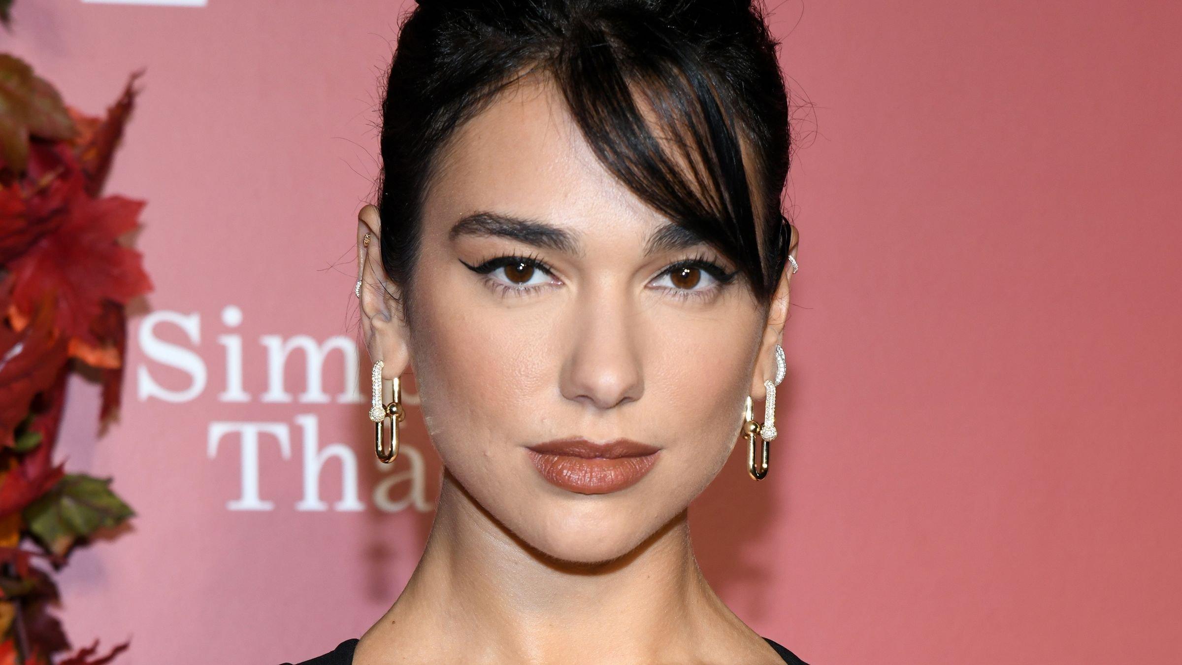 Dua Lipa in strappy black dress with drop-down gold earrings and side-swept bangs.