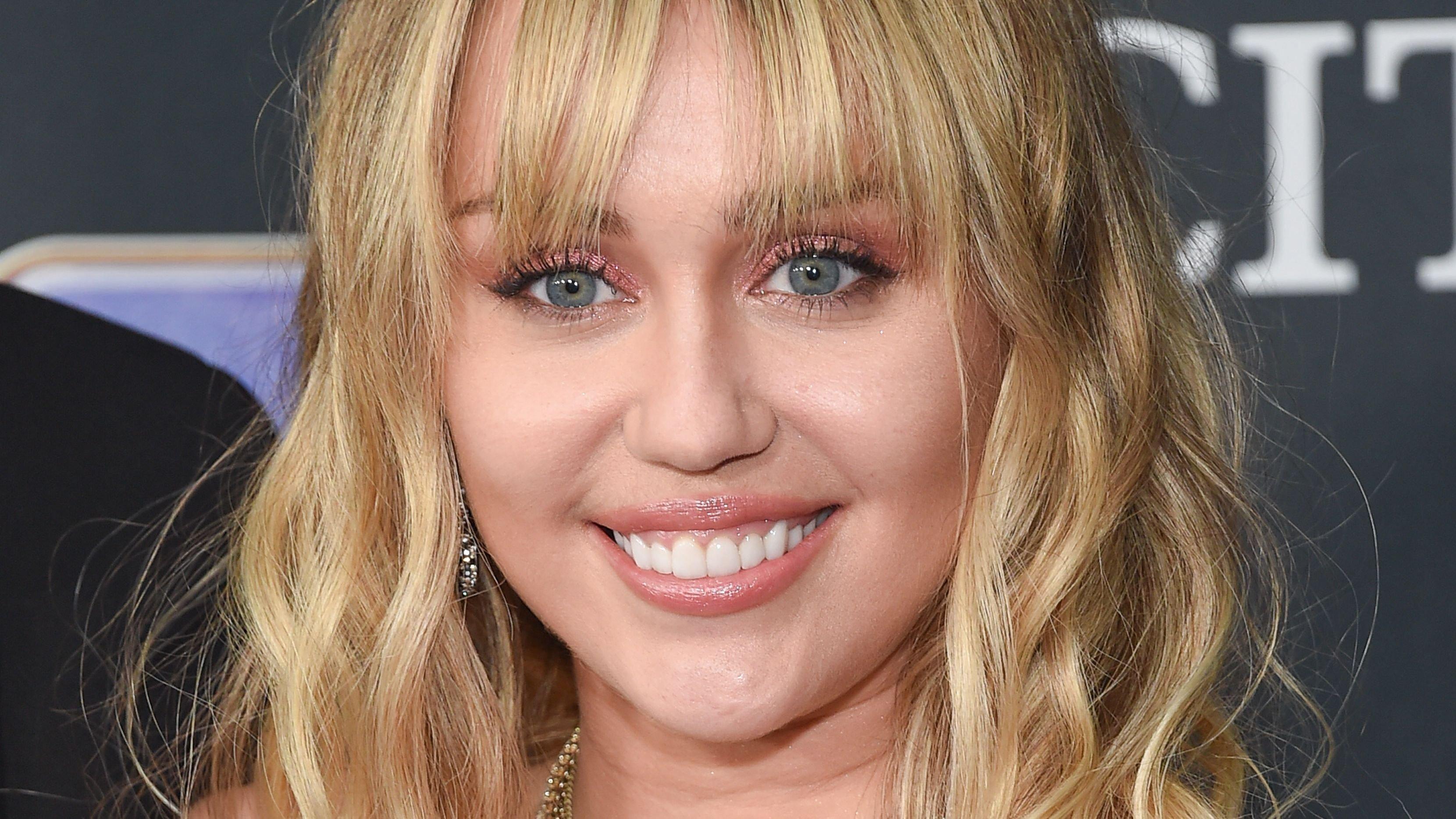 Miley Cyrus sporting bangs and smiling for a photograph.