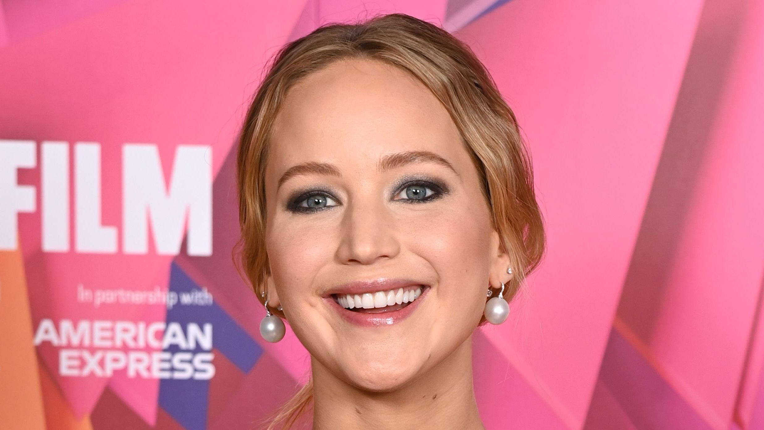 Jennifer Lawrence in black top with white beads and large pearl earrings at an event.