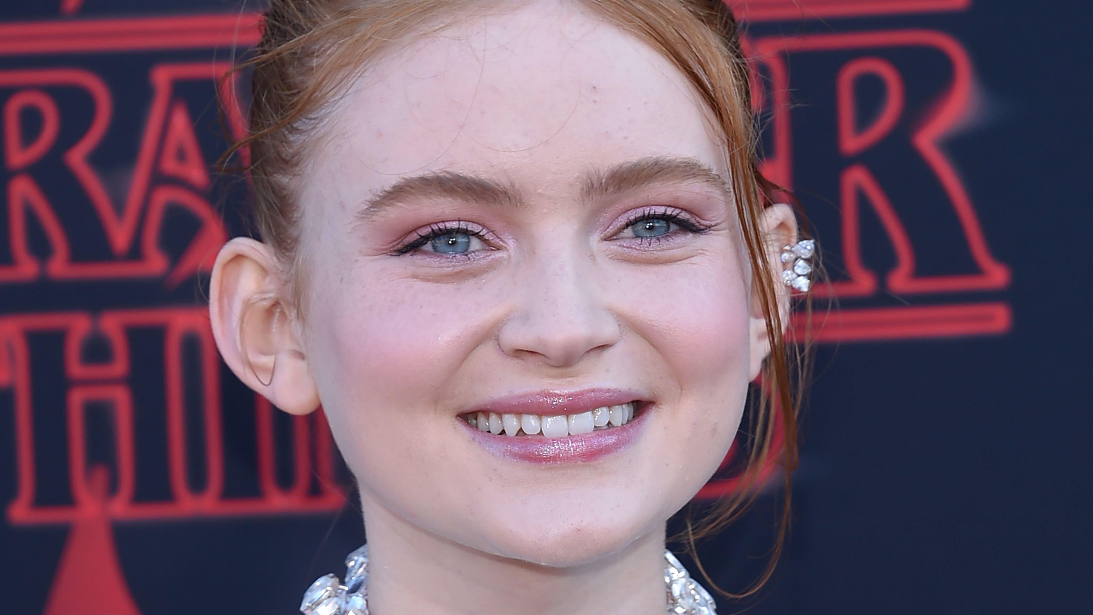 Sadie Sink sporting a tight bun and smiling at the camera.
