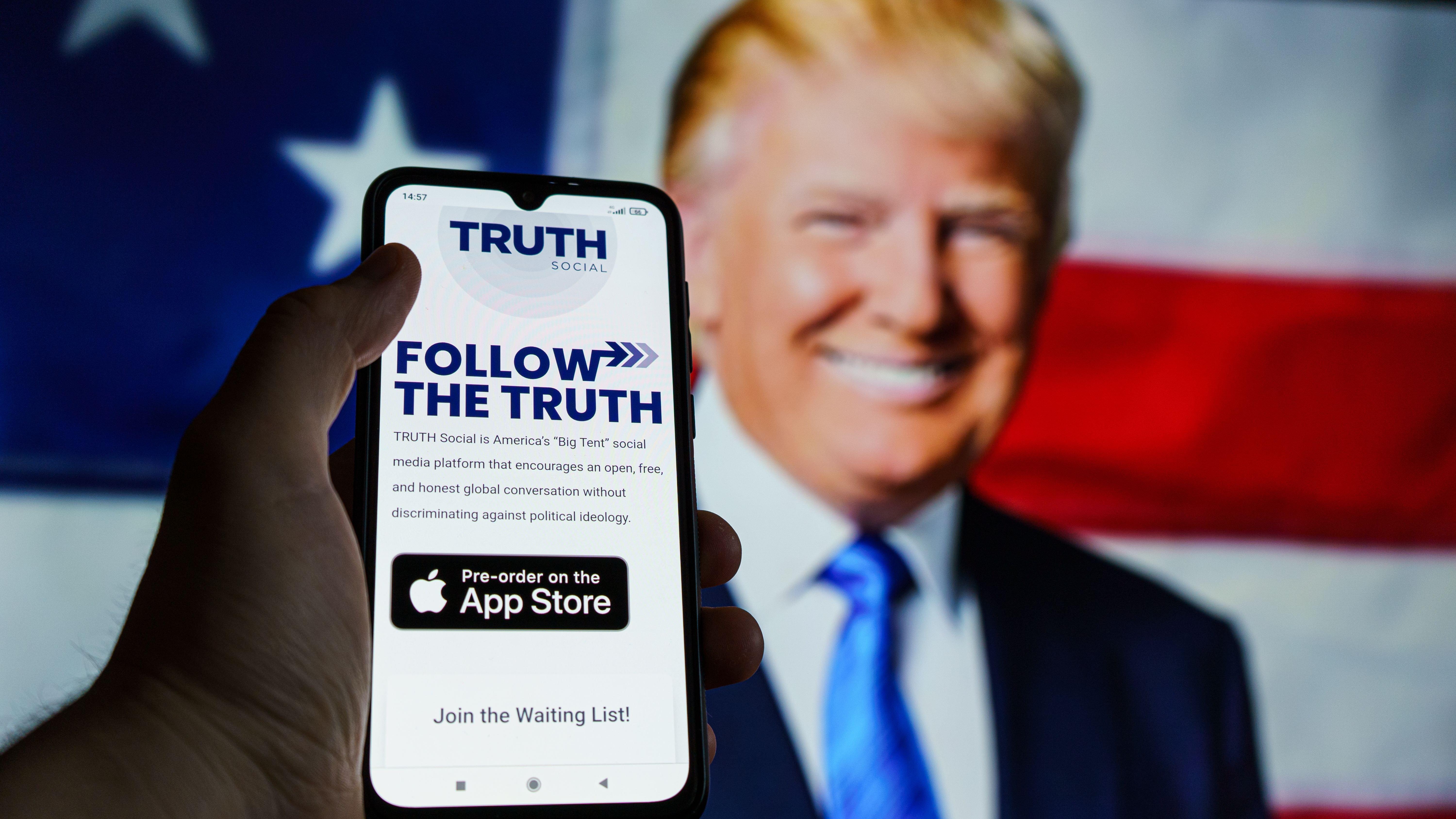 Truth Social app seen on smartphone with Donald Trump in background 