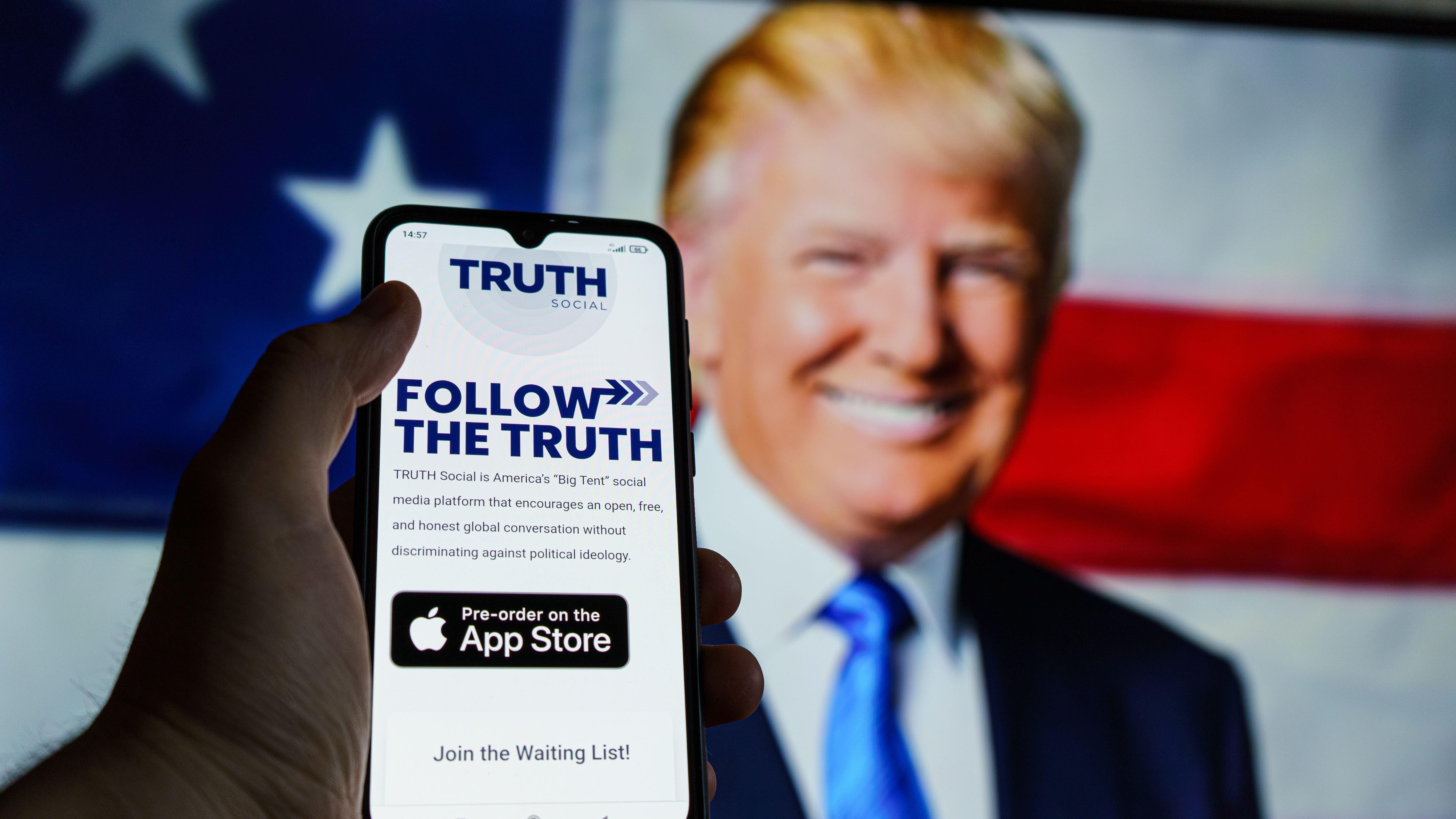The Truth Social app is seen on a smartphone in front of an image of former President Donald Trump