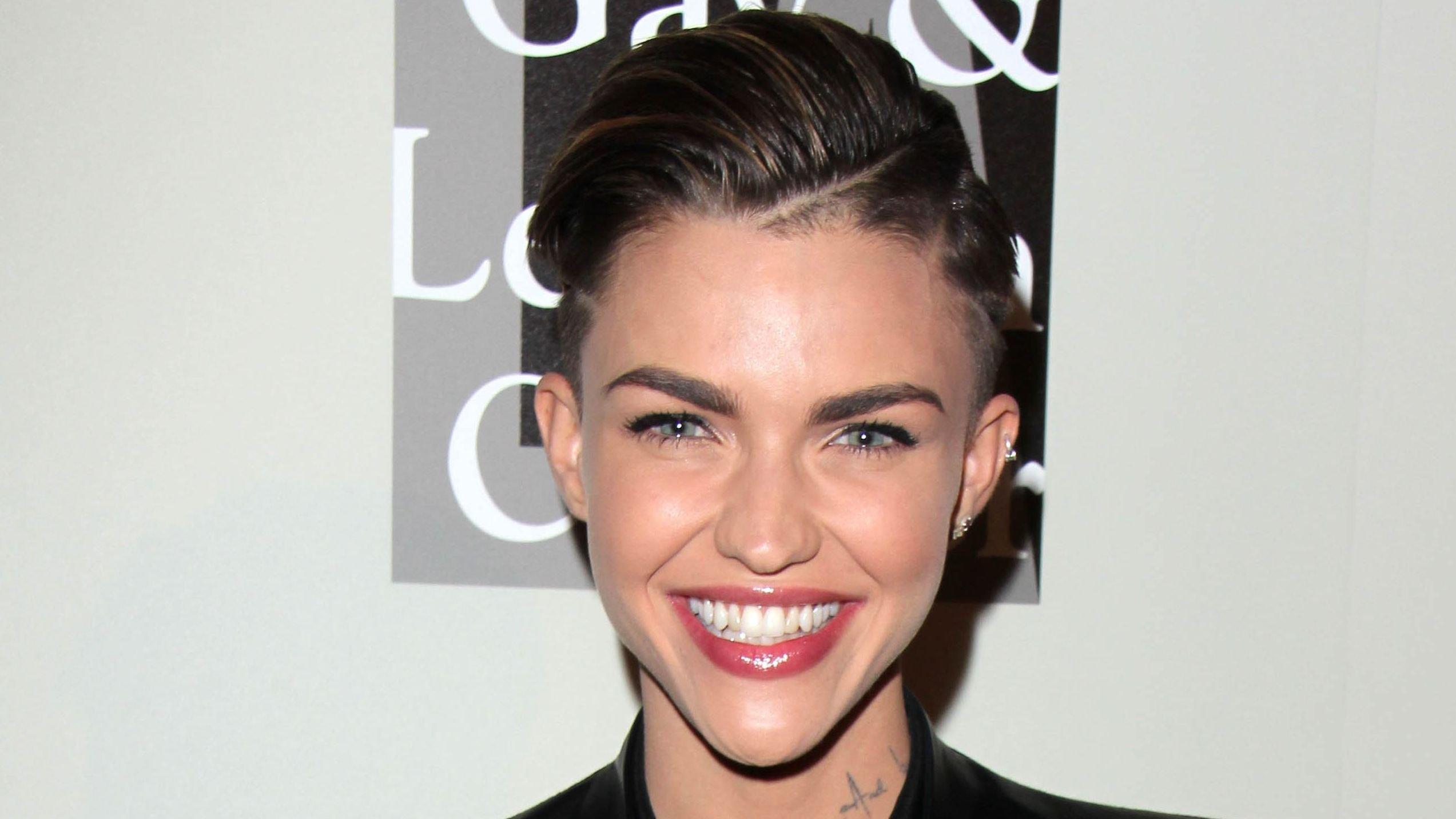 Ruby Rose in all black smiling on a carpet